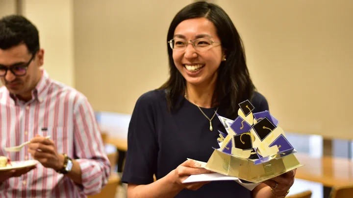 A smiling woman wearing glasses holds a slice of cake decorated with small graduation cap toppers.