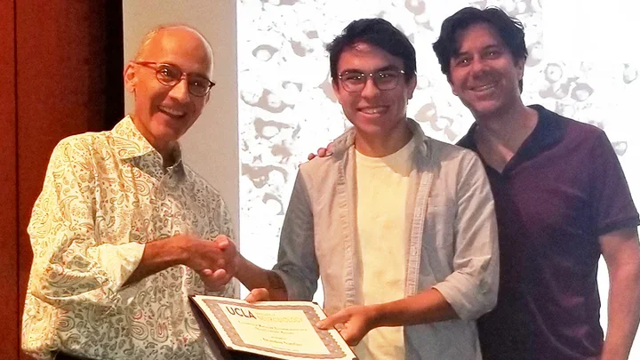 Three men smile for a photo as one of them receives a certificate.