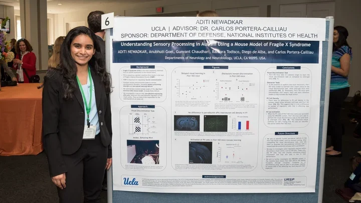 A woman in professional attire stands next to a large academic research poster at a conference.