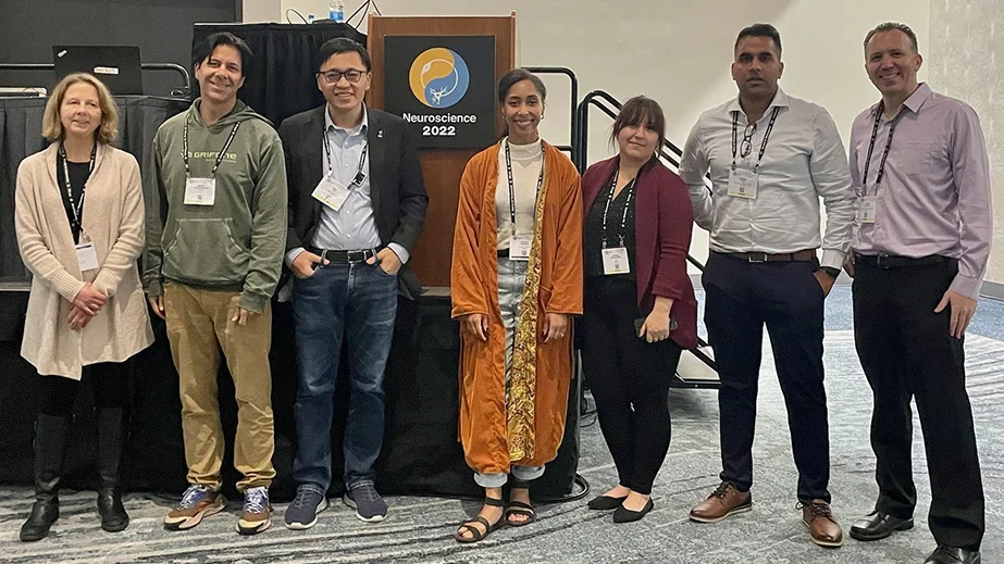 A group of seven people stand side by side in a conference room, posing in front of a podium.