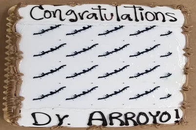 A rectangular cake decorated with the words "Congratulations Dr. Arroyo!" written in black icing.