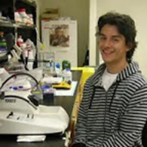 Luis Garza standing at microscope in lab.
