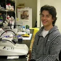 Luis Garza standing at microscope in lab.